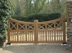 a large wooden gate in front of a brick wall and tree lined area with shrubbery