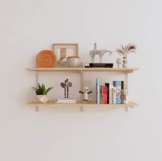 two wooden shelves with books, vases and other decorative items on them against a white wall