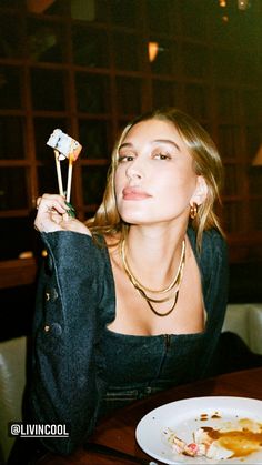 a woman sitting at a table with food in her hand and looking up to the sky