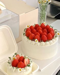 two cakes decorated with strawberries and daisies are on a table next to flowers