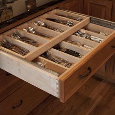 an open drawer in the middle of a kitchen with knives and spoons inside it