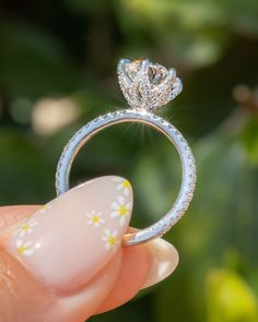 a woman's hand holding a diamond ring in front of her face, with flowers on it