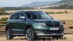 a green suv is parked in the middle of a field with mountains in the background