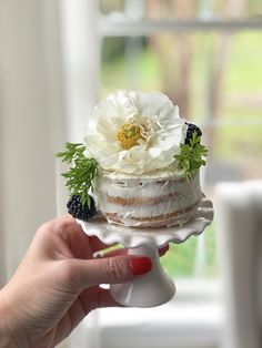 a person holding a cake with flowers on it in front of a window sill