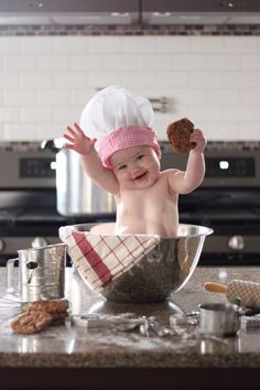 a baby wearing a chef's hat and holding a cookie in a bowl on top of a kitchen counter