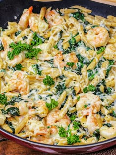 pasta with shrimp and spinach in a skillet on a wooden counter top, ready to be eaten