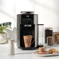 a coffee maker sitting on top of a counter next to some cups and plates filled with food