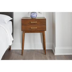 a nightstand with a blue and white vase sitting on it's side next to a bed