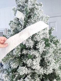 someone is holding a piece of white paper near a christmas tree with snow on it