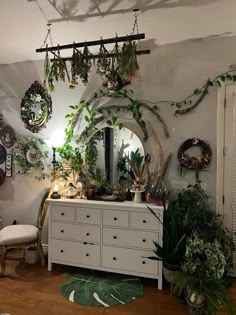 a white dresser topped with lots of potted plants next to a wall mounted mirror