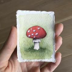 a hand holding up a miniature painting of a mushroom