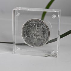 a glass block with a silver coin in it on a white surface next to a green plant