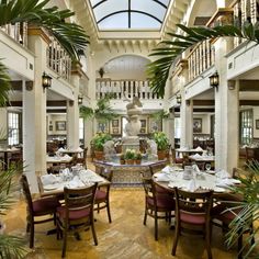 the inside of a restaurant with lots of tables and chairs, plants on either side