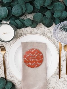 a place setting with napkins, silverware and green leaves on the tablecloth