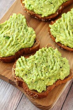 four pieces of bread topped with guacamole on top of a wooden cutting board