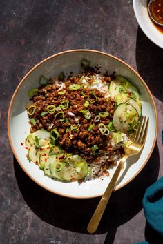 a white bowl filled with rice, meat and cucumbers on top of a table