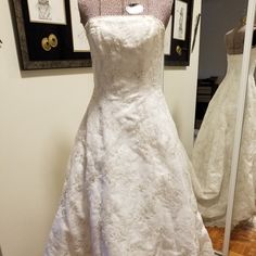 a white wedding dress is on display in front of a mirror and framed pictures behind it