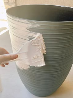 a person holding a paint brush in front of a large gray vase with white stripes