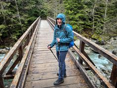 a woman is standing on a bridge with a backpack and walking sticks in her hand