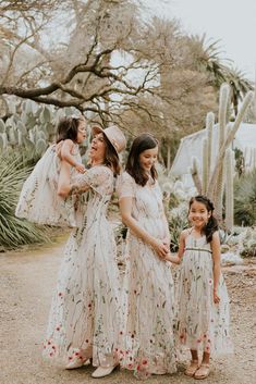 three women in dresses and hats are standing near cacti with cactus trees behind them