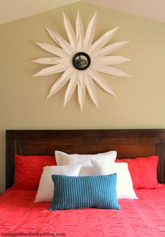 a bed with red sheets and pillows under a large white sunburst on the wall