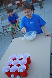 two young boys sitting at a table with cups on it and one boy standing next to the table