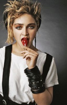 a woman holding a red object in her hand while wearing black bracelets and a white t - shirt