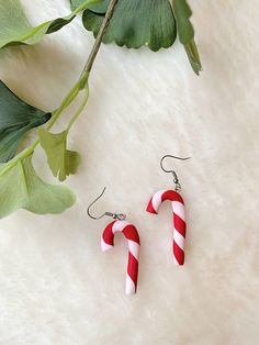 two candy canes are hanging from earrings on a white furnishing next to green leaves