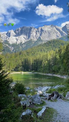 a lake surrounded by trees and rocks with mountains in the background