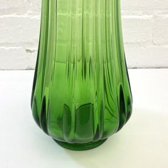 a green glass vase sitting on top of a white table next to a brick wall