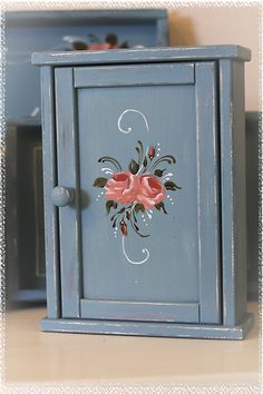 a blue cabinet with pink flowers painted on the front and side doors, sitting on a table