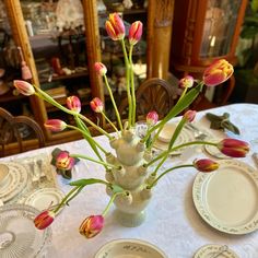 a vase filled with pink and yellow flowers on top of a white table covered in plates