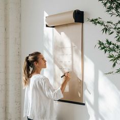 a woman writing on a white board with a black marker in front of her and a plant behind her