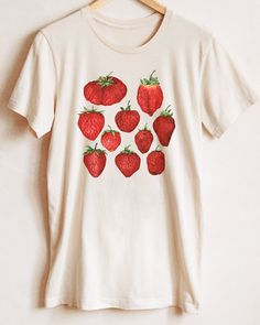 Is it strawberry season yet? These are freshly picked, just for you! T-shirt featuring a botanical illustration of sweet red strawberries, the design you won't find anywhere else. Printed on a natural cream t-shirt, made from durable lightweight cotton. Unisex fit - boxy and long. How it's made: * All prints are original watercolor designs hand-painted by a botanical artist. * Ethically made 100% cotton t-shirts that are made to last. * T-shirts are printed and shipped by my printing partner in the US, Canada, or Europe. * By buying from this shop you are directly supporting a woman-owned small business, created out of love for plants to educate, inspire and keep us connected to the natural world. About the artist: This Shop is an extension of my botanical illustration studio, where I crea Red Fruit Print Top For Spring, Casual Strawberry Print Shirt For Spring, Red Fruit Print Graphic Tee, Red Graphic Tee With Fruit Print, Cotton Shirt With Strawberry Print For Spring, Organic Graphic Print Top For Spring, Organic Tops With Graphic Print For Spring, Spring Fruit Print Graphic Tee Shirt, Spring Fruit Print Graphic Tee