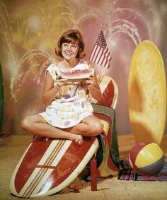 a woman sitting on top of a surfboard with an american flag in front of her