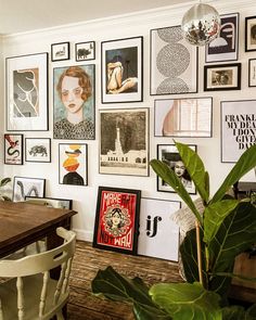 a dining room table with chairs and pictures on the wall above it, along with plants