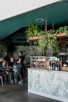 people are sitting at tables with plants hanging from the ceiling and on top of them