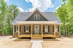 a small gray house in the middle of a wooded area with steps leading up to it's front door