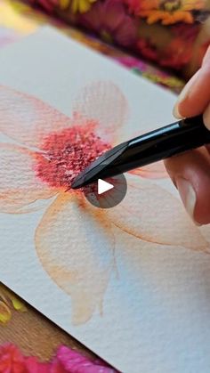 a person is using a pen to draw flowers on a piece of paper with colored pencils