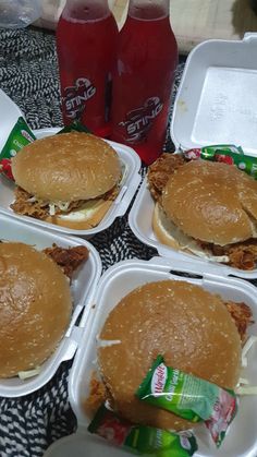 four plastic containers with sandwiches and sodas in them on a black tableclothed surface