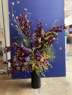 a black vase filled with lots of purple and yellow flowers next to a blue wall