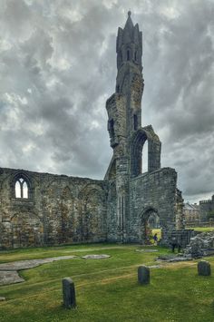 an old stone building with many windows and grass in the foreground on a cloudy day