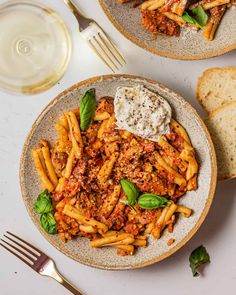 two plates filled with pasta and sauce next to bread on a white counter top,