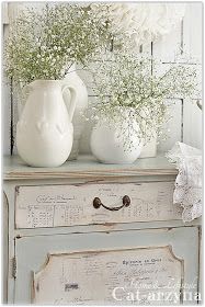 a white vase with flowers on top of an old dresser