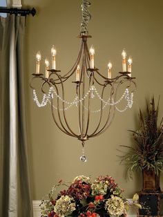 a chandelier hanging over a dining room table with flowers and candles on it