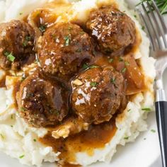 meatballs and gravy over mashed potatoes on a plate with a fork