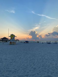 the sun is setting at the beach with lifeguard tower in the foreground and people walking on the sand