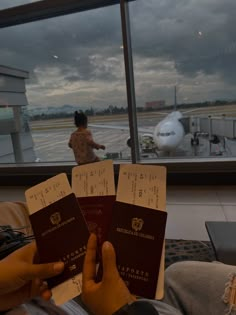 two people are holding up their passports in front of an airport window as the plane is on the tarmac