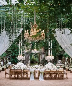 an outdoor wedding reception with chandeliers and white flowers on the table, surrounded by greenery