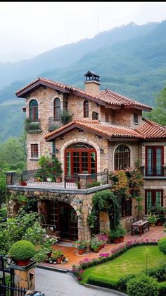 a large house with lots of windows and plants on the front lawn, surrounded by mountains